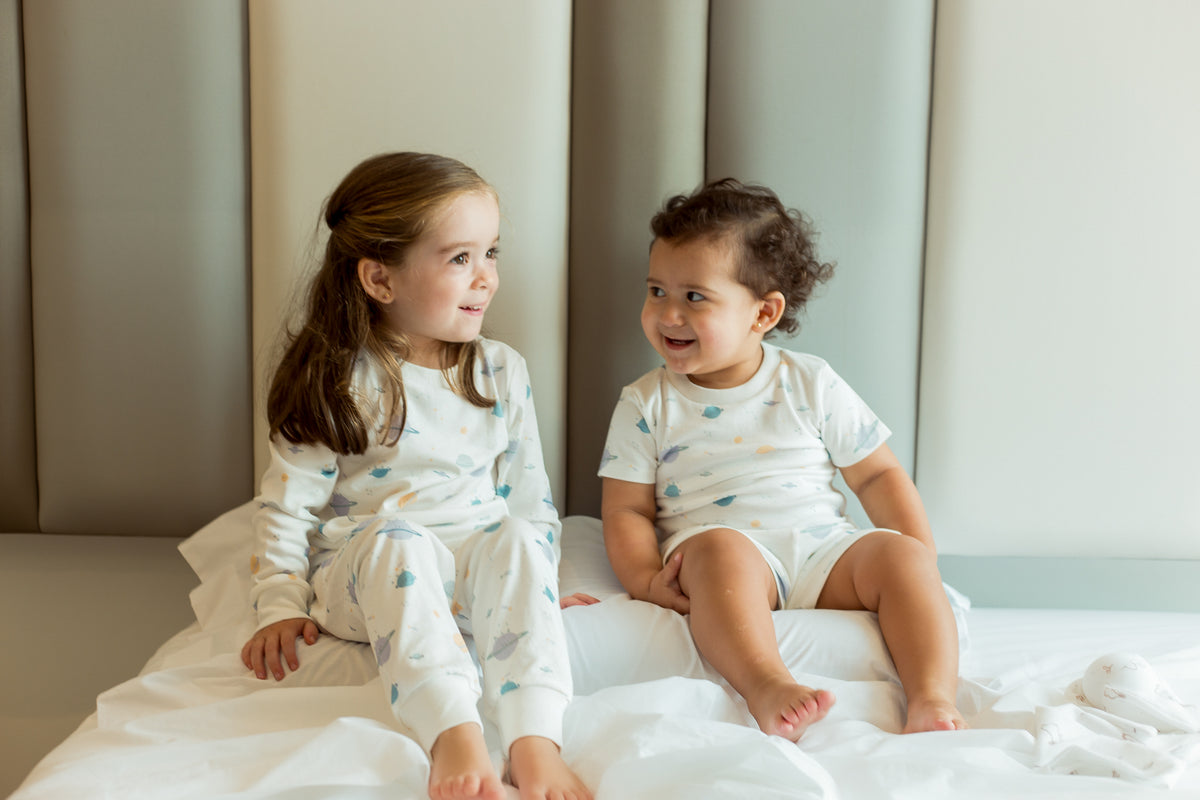 Dos niñas sentadas en la cama con pijamas Clouby de algodón Pima estampado planetas